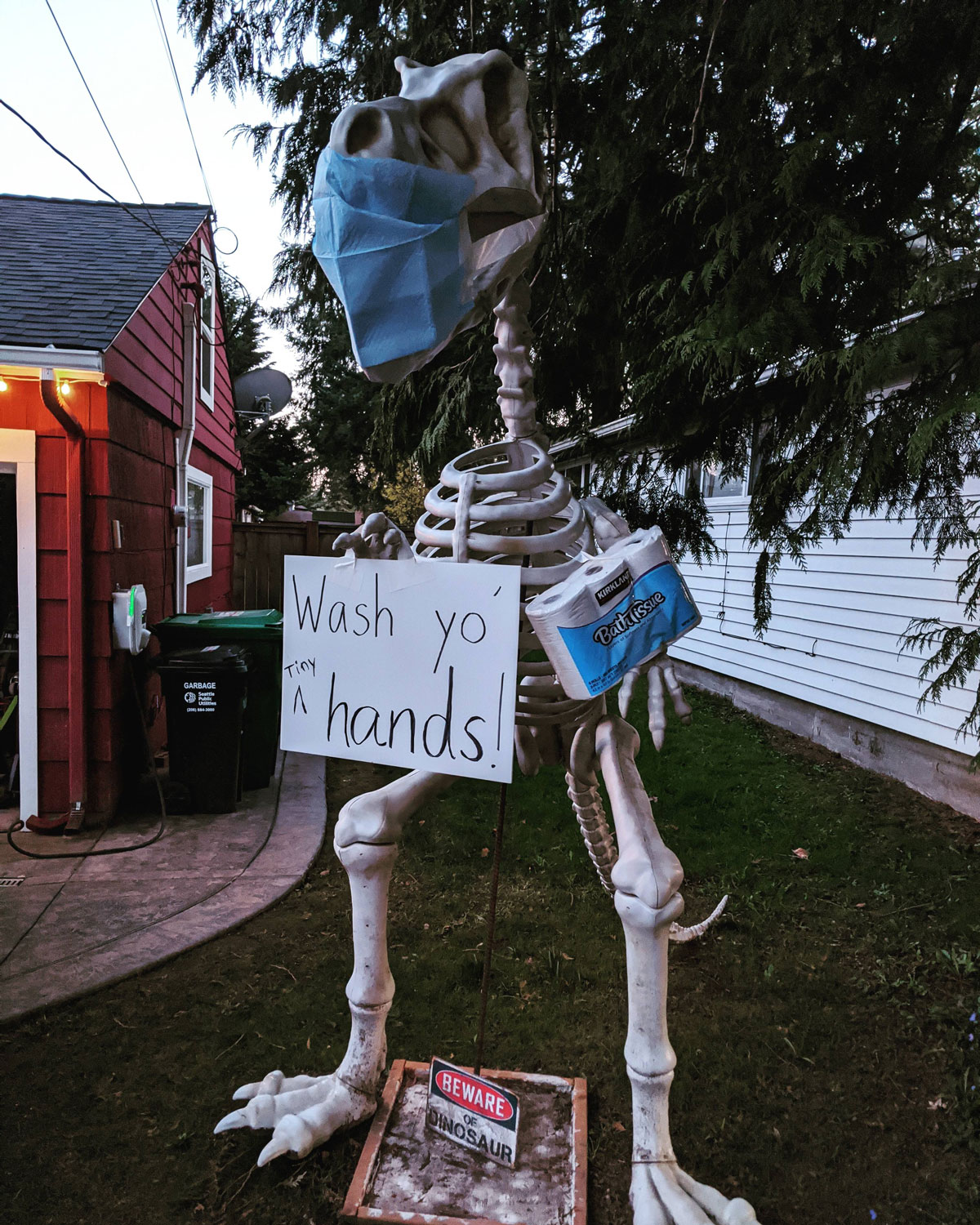 Dinosaur skeleton wearing a mask with a sign that says 'Wash yo' hands!'